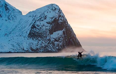 A surfer rides a wave at the snowy beach of Unstad, in Lofoten Island, Arctic Circle, on March 9, 2016. Surfers from all over the world comes to Lofoten island to surf in extrem conditions. Ocean temperature is 6-7 °C, air temperature around 0°C in spite of a weather very unstable. / AFP PHOTO / OLIVIER MORIN