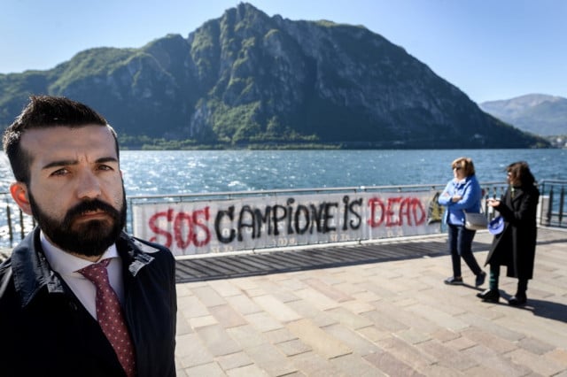 Union representative Vincenzo Falanga poses next to a banner that reads 'SOS Campione is dead' in the Italian enclave of Campione d'Italia in Switzerland. Photo: FABRICE COFFRINI / AFP