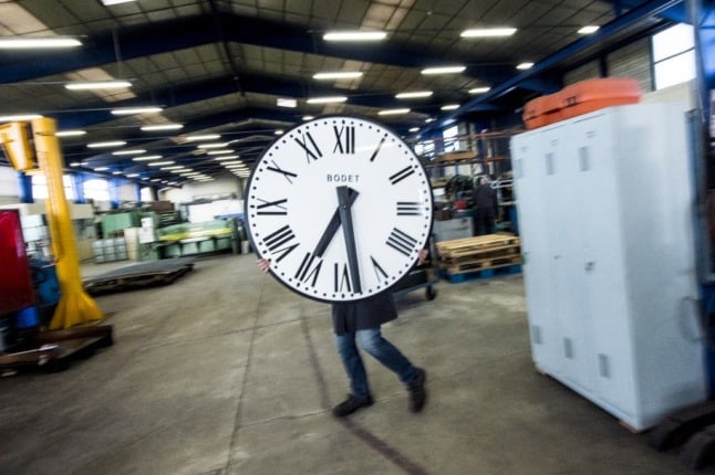 A factory worker moves a clock.