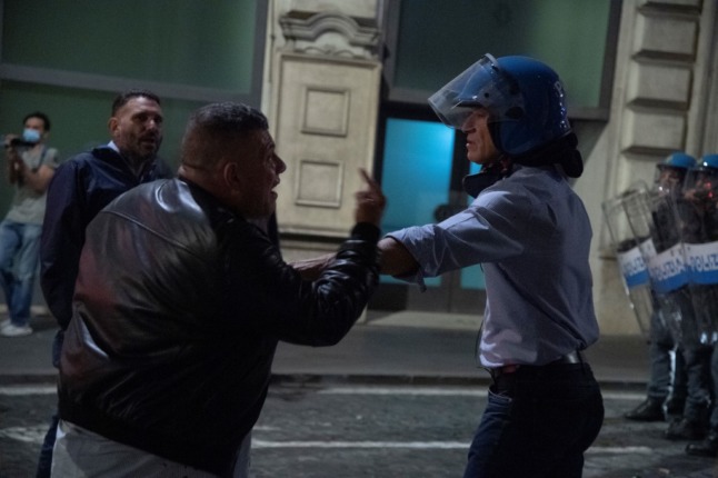 A protester rudely gesticulates at a policeman during protests against Italy's 'green pass'. 