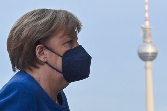 Side profile of Angela Merkel in a protective face mask with the Berlin TV tower in the background.
