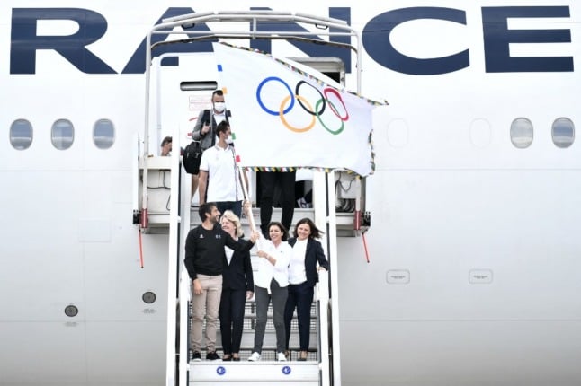 Delegates of the Paris 2024 Olympic Games stand at the entrance to an Air France passenger jet, waving the Olympic flag