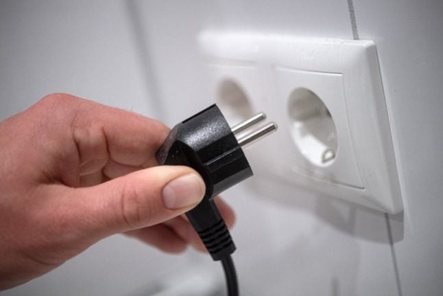 A man places a plug into the wall. 