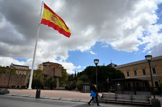 A Spanish flag flutters as a woman wearing a face mask walks in Madrid on April 2, 2020 amid a national lockdown to fight the spread of the COVID-19 coronavirus. - The coronavirus death toll in Spain surged past 10,000 after a record 950 deaths in 24 hours, with the number of confirmed cases passing the 110,000 mark, the government said. (Photo by Gabriel BOUYS / AFP)