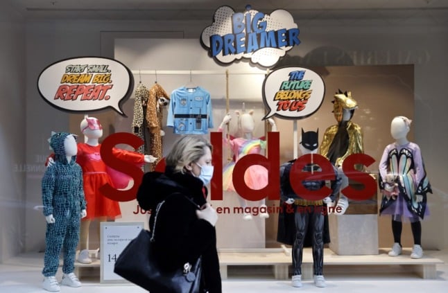 A woman wearing a facemask walks past a storefront advertising discounts, on the first day of the winter sales in France