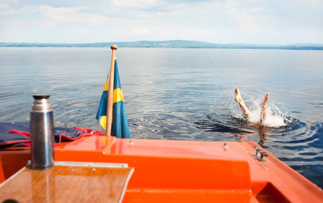 a person diving into a lake in Sweden, it's summer and you can see the Swedish flag on a boat