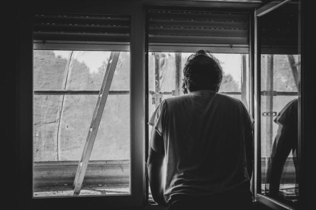 Black and white photo of man looking out of partially opened window.