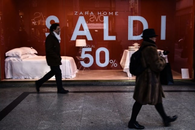People walk past a shop advertising the winter sales in Italy.