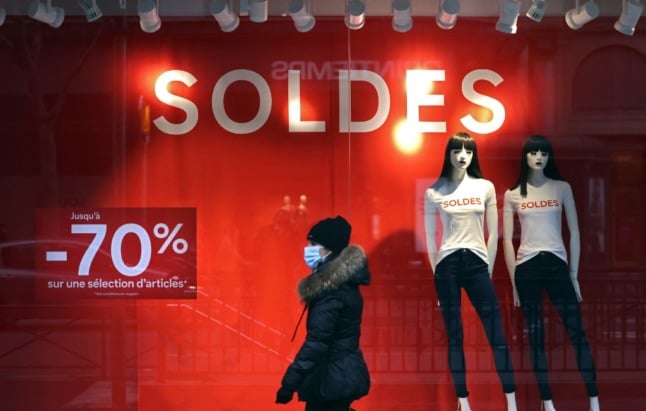 A woman walks past a shopfront advertising sales in France.