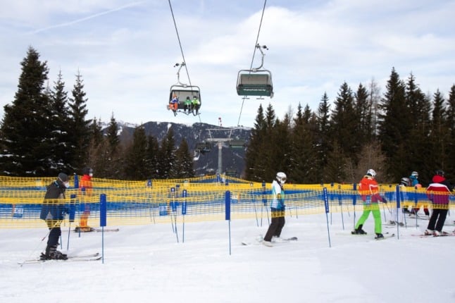 A skier wearing a FPP 2 mask stands in front of a warning sign before the cue to board the ski lift in the ski resort Stuhleck