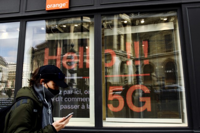 A masked man talks on a mobile phone as he walks past a store belonging to French telecom group Orange