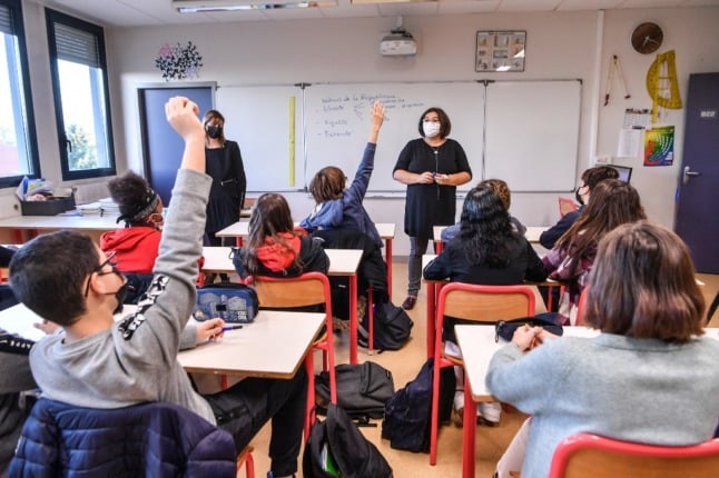 Pupils wearing facemasks raise their hands to respond to a question from a teacher